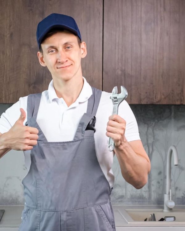 plombier-masculin-positif-uniforme-montre-pouce-vers-haut-tenant-cle-plomberie-dans-locaux-cuisine-services-reparation-plomberie-dans-appartements